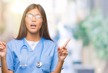 Young asian doctor woman over isolated background amazed and surprised looking up and pointing with fingers and raised arms.