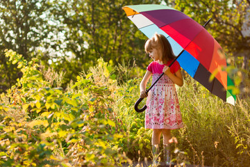 Happy child girl walk with multicolored umbrella under rain