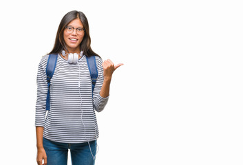 Young asian student woman wearing headphones and backpack over isolated background smiling with happy face looking and pointing to the side with thumb up.