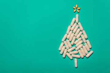Top view of white capsules and yellow pills forming a Christmas tree on green background with copy space. Medical or pharmacy holiday background