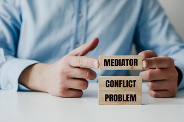 Businessman in a blue shirt arranges wooden jigsaw blocks with the word CONFLICT, MEDIATOR. Problem...