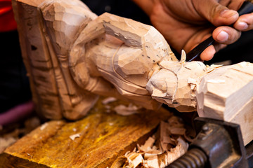 Closeup of a carpenter's hands working with a chisel and hammer on wooden buddha sculpture - obrazy, fototapety, plakaty