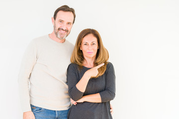 Beautiful middle age couple in love over isolated background Pointing with hand finger to the side showing advertisement, serious and calm face