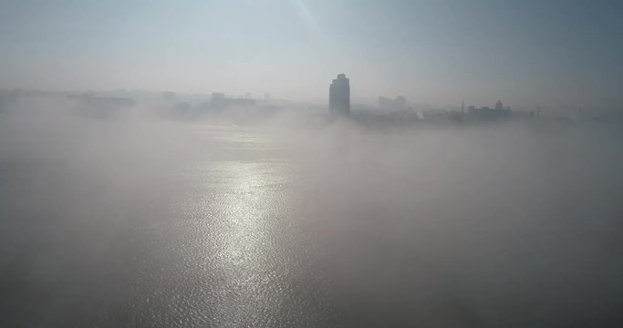 A huge barge on the river Dnipro in the morning fog with a visible silhouette of the buildings and city in the background (shot from the air) in 4K 8