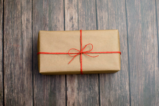 Gift box wrapped in recycled paper with red twine on wood background.