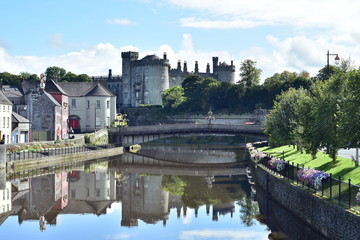 View of calm river Nore with bridge and stone Kilkenny Castle in background. - obrazy, fototapety, plakaty