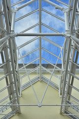 White painted steel structure of passage roof with glass panes and blue sky in background.