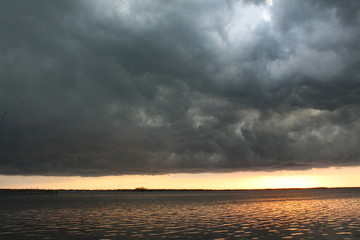 Thick dark gray storm clouds over the water at sunset
