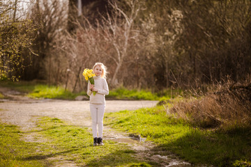 cute blonde happy little girl with yellow daffodils in the spring country