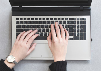 Business woman typing on a laptop keyboard on gray background, top view, hands close up