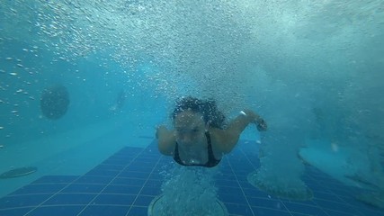 Cute girl diving underwater through bubbles in aquapark.