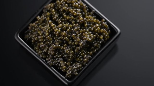 Black Caviar closeup. Natural sturgeon black caviar in square dish rotated on black background, rotation. Delicatessen. Slow motion. 3840X2160 4K UHD video footage