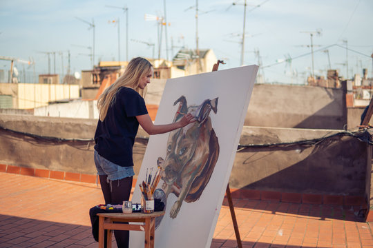 Young woman paint artist drawing at home roof. Picture of bulldog on big canvas. Outdoors art