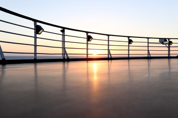 Railing and deck flooring of a cruise ship at sunset with the ocean in the background.