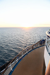 Railing and deck flooring of a cruise ship at sunset with the ocean in the background.