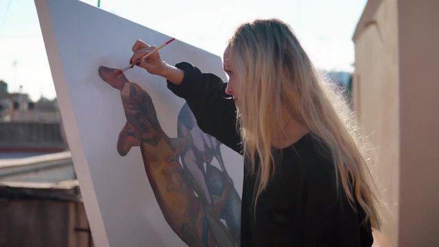 Young woman paint artist coming for drawing at home roof. Picture of bulldog on big canvas. Outdoors art