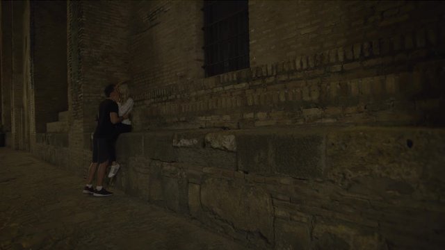 Romantic couple leaning on building hugging and kissing at night / Seville, Sevilla, Spain