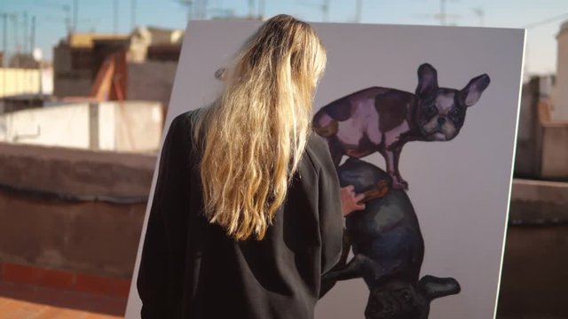 Young woman paint artist coming for drawing at home roof. Picture of bulldog on big canvas. Outdoors art