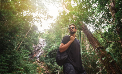 Handsome young stylish man in black t-shirt and sunglasses is engaged in trekking in the green...