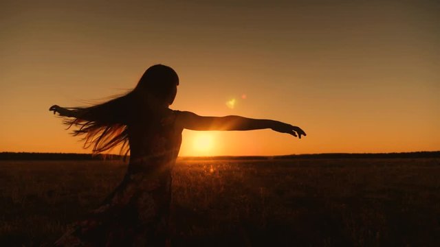 Silhouette of girl with long disheveled hair whirls in flight in glare of setting sun and smiles. Free and romantic woman.