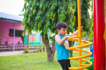 Obraz premium Active Asian Kid playing climbing metal spiral at school yard playground. Kids play and climb outdoors.
