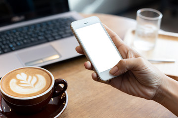 hand woman using a telephone, empty screen smart phone and computer on wooden table In the coffee shop. with clipping path