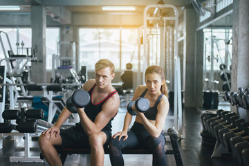 Fototapeta premium Sporty man and woman exercise with dumbbells,Couple sport people in sportswear does the exercises at gym