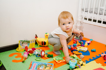 The happy little girl shows and plays a lot of toys on colored mat and puzzles, the white background in the room. Close up. Infant. emotions of amazement.