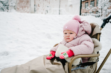 A little girl sitting in childrens sled in the park. Close up. Happy family walking in the park. Portrait Infant.