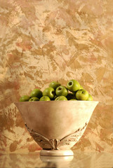 A bowl of green apple fruit on an interesting gilded background