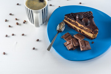 A piece of chocolate cake, and pieces of chocolate on a blue plate, next to a cup of coffee, on a light wooden background.