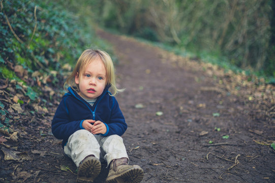Little toddler resting on a path in the woods
