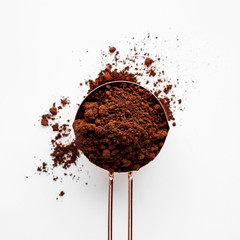 Rose gold measuring cup of cocoa powder on a white background, healthy food concept