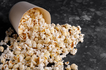 Snack for watching movies. Popcorn fallen out of a paper bucket on a textural background.