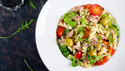 Pasta salad with tuna, tomatoes, olives, cucumber, sweet pepper and arugula on rustic background ....