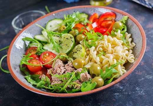 Buddha bowl. Pasta salad with tuna, tomatoes, olives, cucumber, sweet pepper and arugula on rustic background .