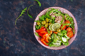 Fototapeta na wymiar Tuna salad with tomatoes, olives, cucumber, sweet pepper and arugula on rustic background . Top view