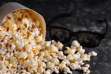 Snack for watching movies. A bucket of popcorn on a dark background and glasses.