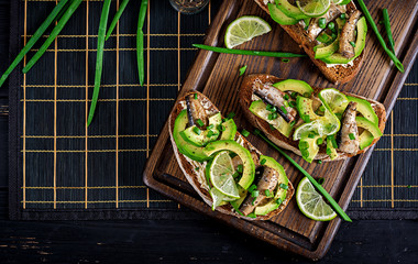 Sandwich - smorrebrod with sprats, avocado and cream cheese on wooden board. Danish cuisine. Top view