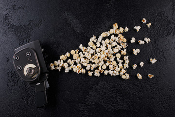 Obraz na płótnie Canvas Retro movie camera with popcorn flying out of it on a dark background.