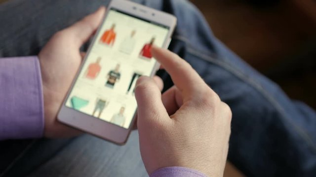 A man looks at the goods in the online clothing store. People using Smartphone, online shopping. The screen is blurred. Close-up. 4K UHD.