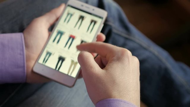A man looks at the goods in the online clothing store. People using Smartphone, online shopping.  The screen is blurred.  Close-up. 4K UHD.