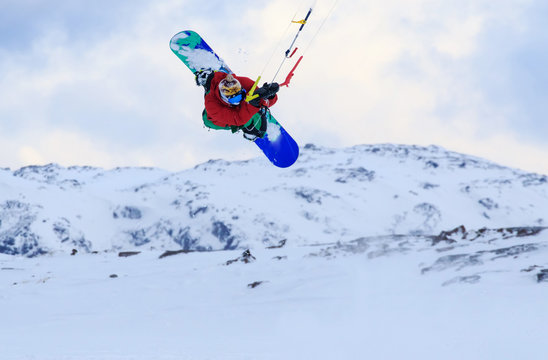 Professional kite boarding rider sportsman with kite in sky jumps high acrobatics kiteboarding trick with grab of kiteboard. Recreational activity, extreme active sports, snowkiting ski snowboard