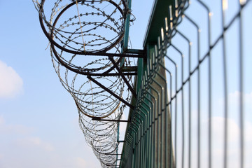 Steel fence with metal barb construction on blue sky background. Barbwire secure border. Outdoor...