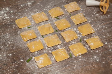Tasty raw ravioli with flour on wooden background. Process of making italian ravioli. Selective focus