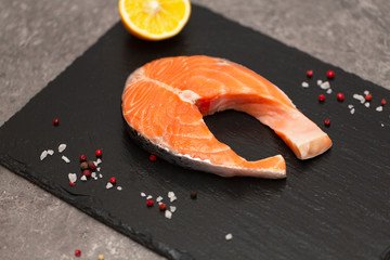 Fresh salmon steak with spices and lemon on a black slate plate