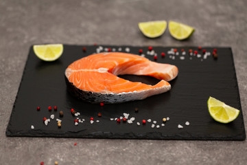 Salmon steak raw fish prepared for cooking with lime and spices. Top view on black slate board.