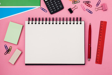 Open school notebook for your text over colorful supplies on pink background. Back to school concept with copy space. Flat lay. Top view.