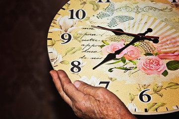 Old grandmother holding a ticking clock closeup