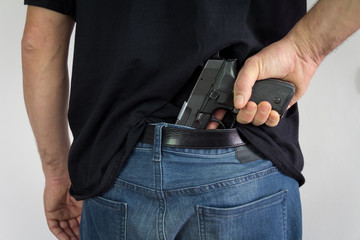 The man holding the gun in his hand behind his back. Illegal possession of weapons